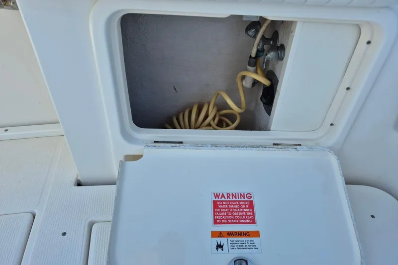 Slide: The Image of Open storage compartment on 2004 Riviera 4000 Offshore boat with coiled hose and warning label. - 11