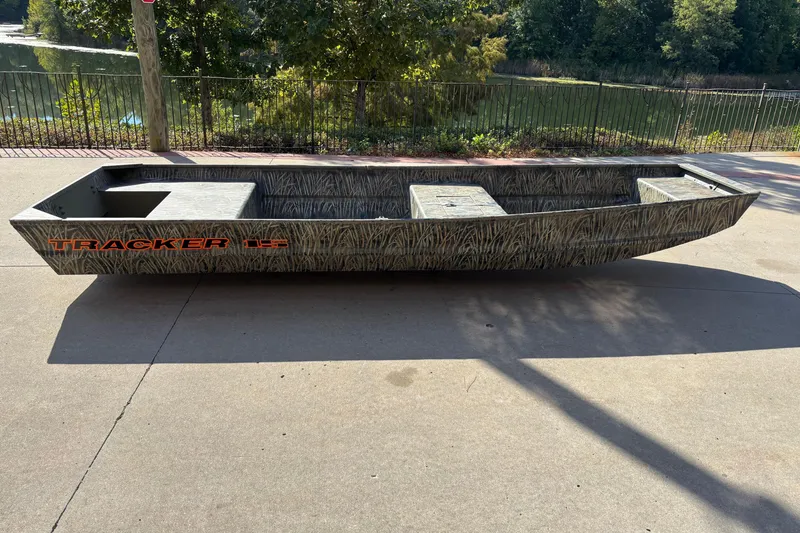 The Image of 2026 Tracker Grizzly 15 Jon boat on pavement, camo design, near a scenic lake. - 0