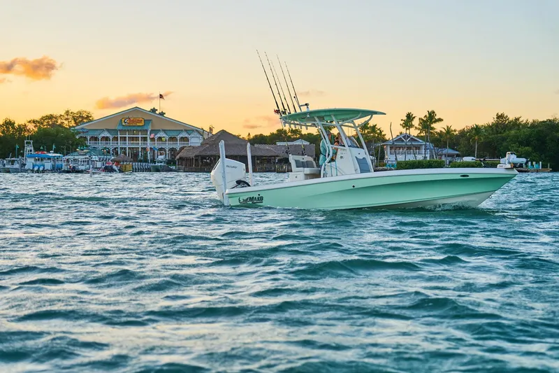 Slide: The Image of 2026 Mako 24 APEX boat on water at sunset near a coastal building. - 56