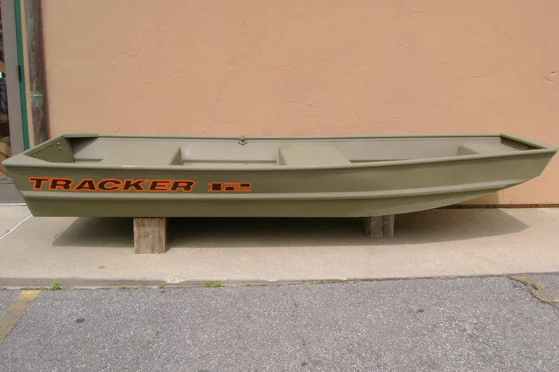 The Image of 2026 Tracker Grizzly 12 Jon boat in olive green, displayed outdoors on wooden blocks. - 0
