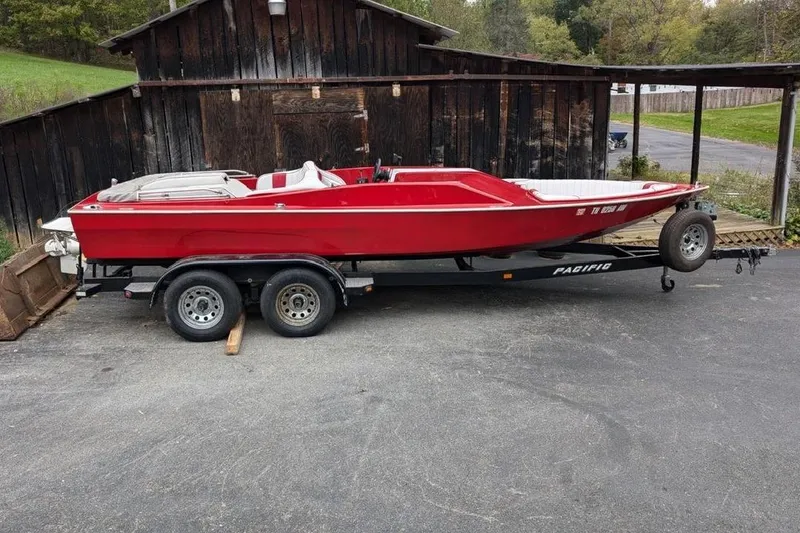 Slide: The Image of 1975 Sleekcraft Executive 23 red boat on trailer, parked by rustic wooden building. - 5