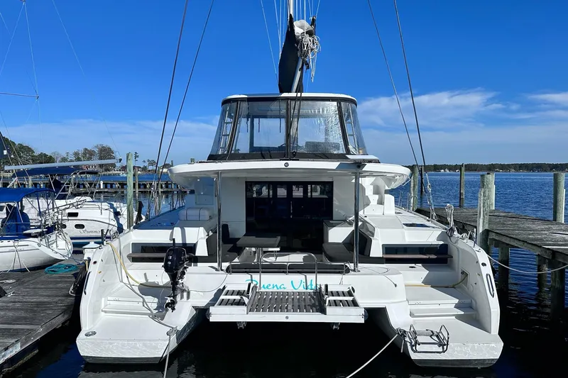 Slide: The Image of 2023 Lagoon 50 catamaran docked at a marina under clear blue skies. - 2