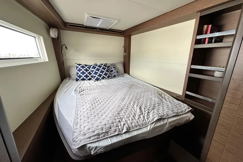 Slide: The Image of 2023 Lagoon 50 yacht cabin with cozy bed, window, and built-in shelves. - 31