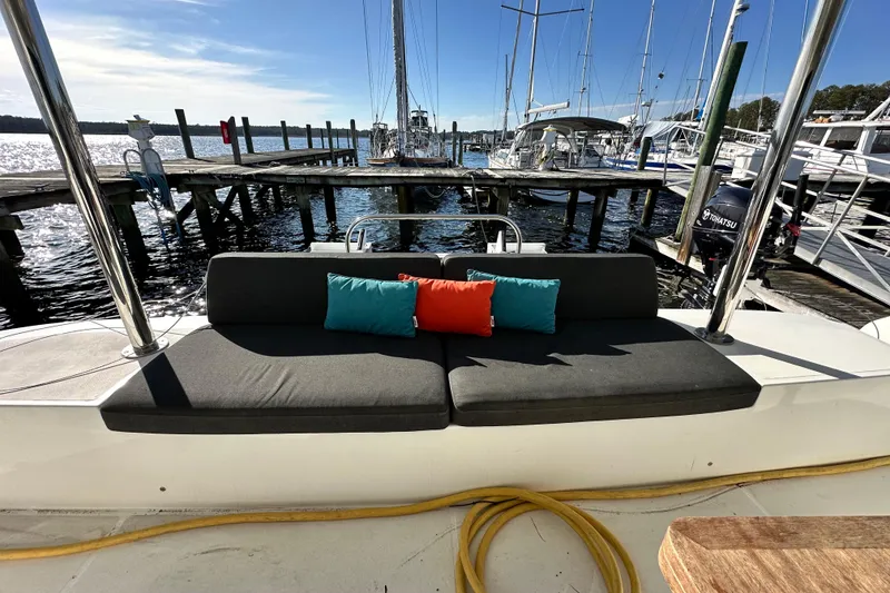 Slide: The Image of 2023 Lagoon 50 yacht with cushioned seating and colorful pillows at a marina. - 38