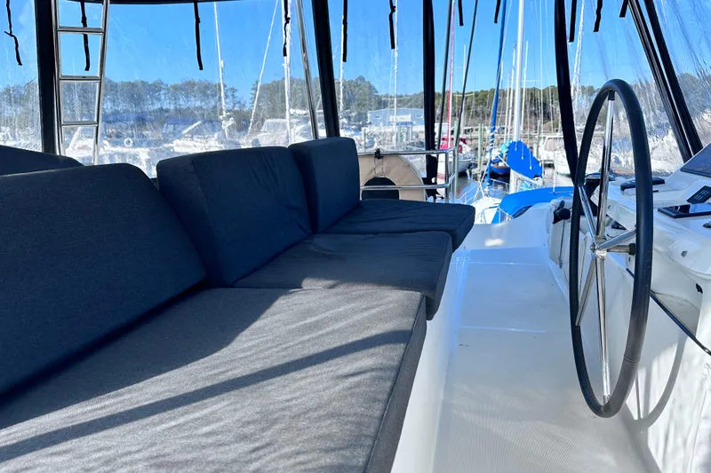 Slide: The Image of 2023 Lagoon 50 yacht cockpit with cushioned seating and steering wheel, docked at marina. - 6