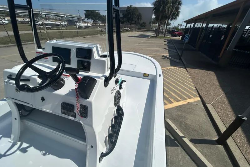 Slide: The Image of 2026 Shallow Sport 18 Sport boat console with steering wheel and controls in a parking area. - 11