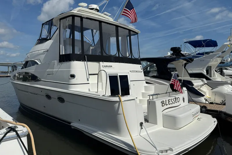 The Image of 2004 Carver 444 Cockpit Motor Yacht docked, displaying American flags and "Blessed" on the stern. - 0