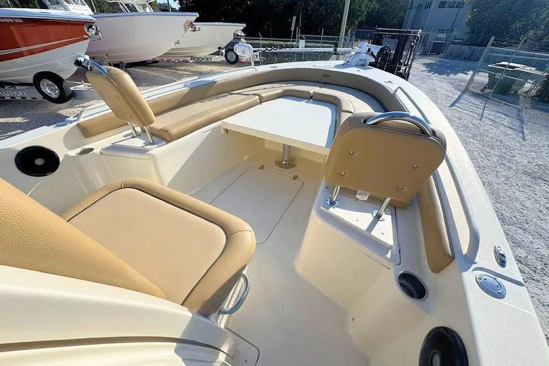 Slide: The Image of 2016 Scout 251 XS boat interior with tan seating and table, parked outdoors. - 11