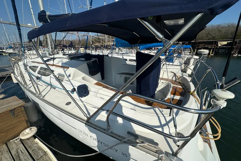 Slide: The Image of 2004 Jeanneau Sun Odyssey 35 sailboat docked at marina, featuring spacious cockpit and blue canopy. - 2