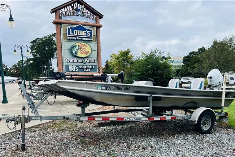 The Image of 1985 Grumman Outlaw boat on trailer near shopping center signs. - 1