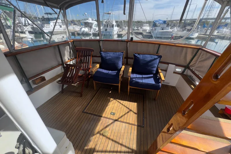 Slide: The Image of 1966 Grand Banks 32 Sedan boat deck with wooden chairs and blue cushions, docked at marina. - 24
