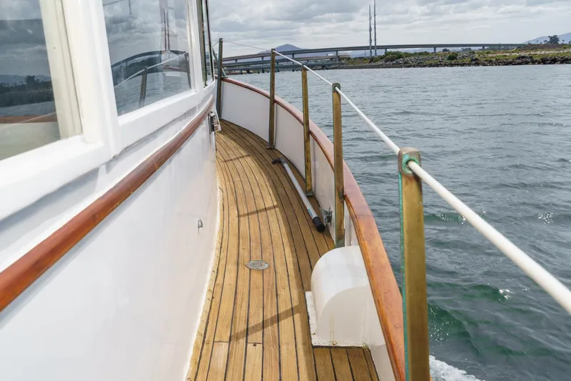 Slide: The Image of 1966 Grand Banks 32 Sedan boat deck with wooden railings on a calm waterway. - 66