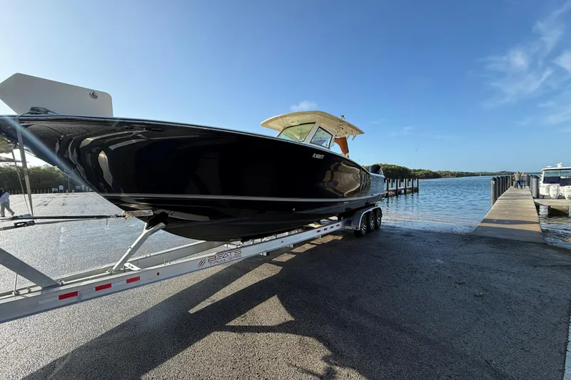 Slide: The Image of 2019 Scout 355 LXF boat on trailer near water under clear blue sky. - 13