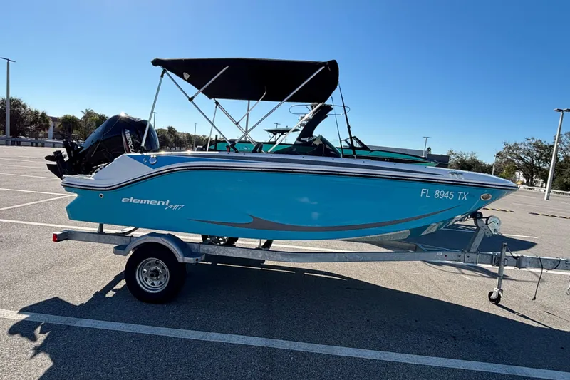 Slide: The Image of 2023 Bayliner Element M17 boat on trailer in parking lot, blue hull, black canopy. - 4
