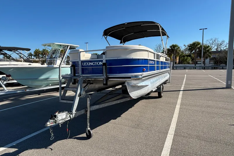 Slide: The Image of 2023 Lexington 321 Fish pontoon boat on trailer in sunny parking lot. - 2