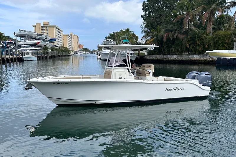 The Image of 2020 NauticStar 25 XS boat on a calm waterway, surrounded by buildings and palm trees. - 0