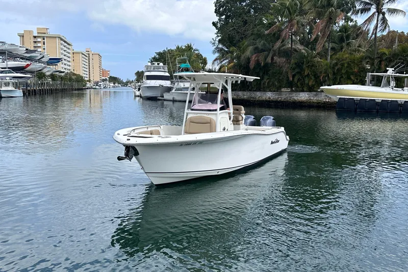 Slide: The Image of 2020 NauticStar 25 XS boat cruising in a scenic waterway with palm trees and buildings. - 13