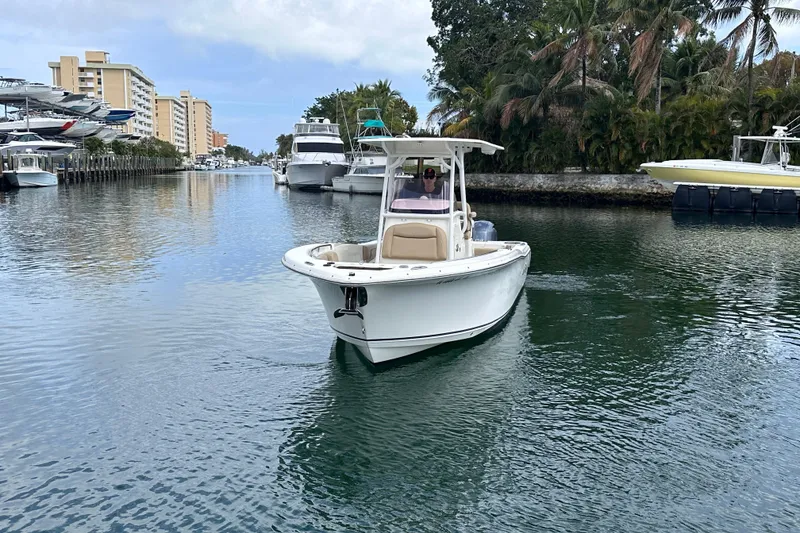 Slide: The Image of 2020 NauticStar 25 XS boat cruising in a scenic waterway with palm trees and buildings. - 15
