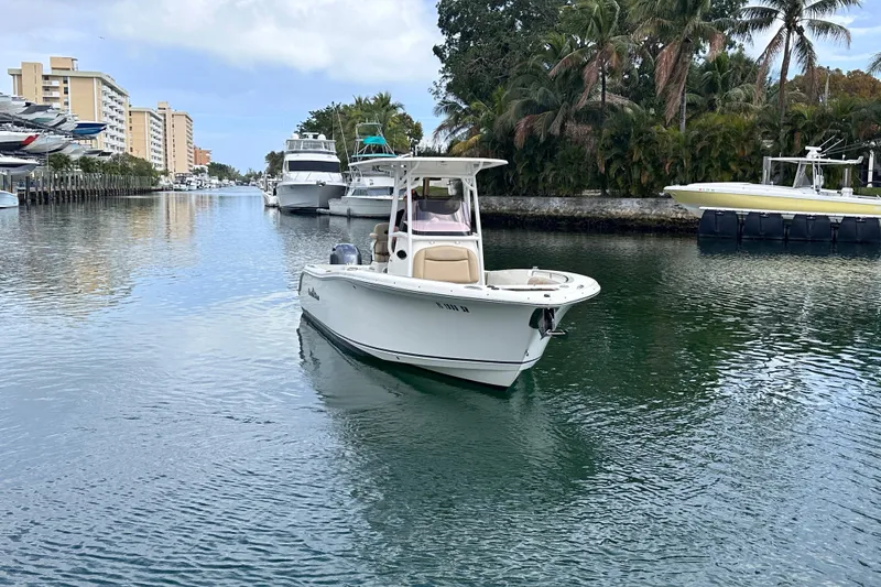 Slide: The Image of 2020 NauticStar 25 XS boat cruising in a scenic canal with palm trees and yachts. - 19