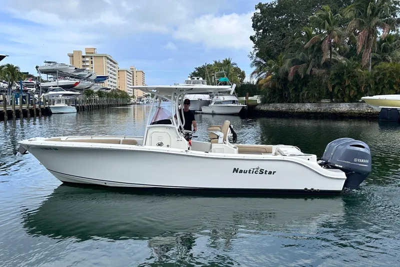 Slide: The Image of 2020 NauticStar 25 XS boat cruising in a marina with lush greenery and buildings. - 2