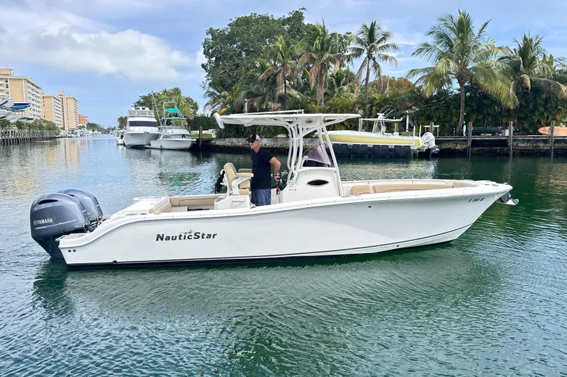 Slide: The Image of 2020 NauticStar 25 XS boat on calm water, surrounded by palm trees and buildings. - 26