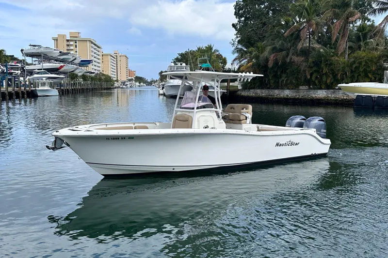 Slide: The Image of 2020 NauticStar 25 XS boat cruising in a scenic waterway with palm trees and buildings. - 8