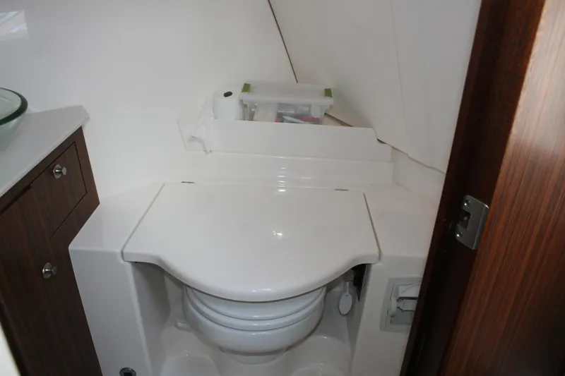 Slide: The Image of 2016 Pursuit OS 325 Offshore boat bathroom with compact toilet and wooden cabinetry. - 19