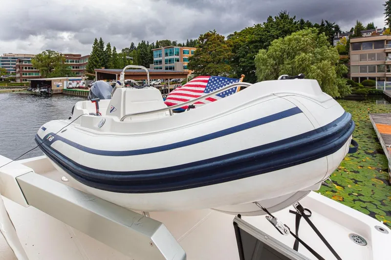 Slide: The Image of 2004 West Bay Sonship yacht with inflatable boat, docked near lush greenery and buildings. - 27