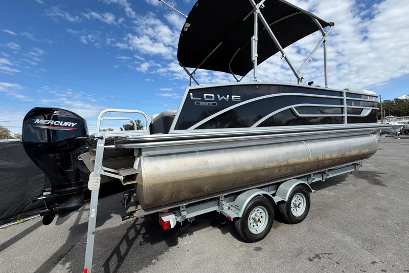 Slide: The Image of 2023 Lowe SS 210 pontoon boat with Mercury engine on trailer under blue sky. - 2