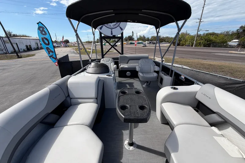 Slide: The Image of 2023 Lowe SS 210 pontoon boat interior with seating and table, parked outdoors. - 33