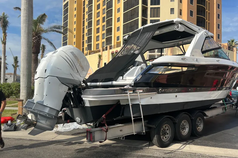 Slide: The Image of 2023 Four Winns H350 OB boat on trailer near tall building and palm trees. - 3