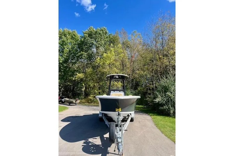 Slide: The Image of 2023 Sportsman Open 232 Center Console boat on trailer, surrounded by trees and blue sky. - 2