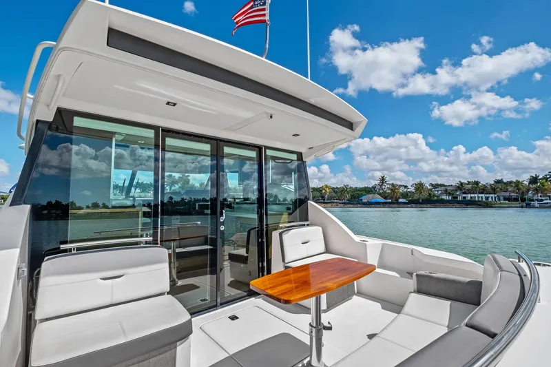 Slide: The Image of 2018 Tiara Yachts C44 Coupe, luxury yacht deck with seating and table, scenic waterfront view. - 32