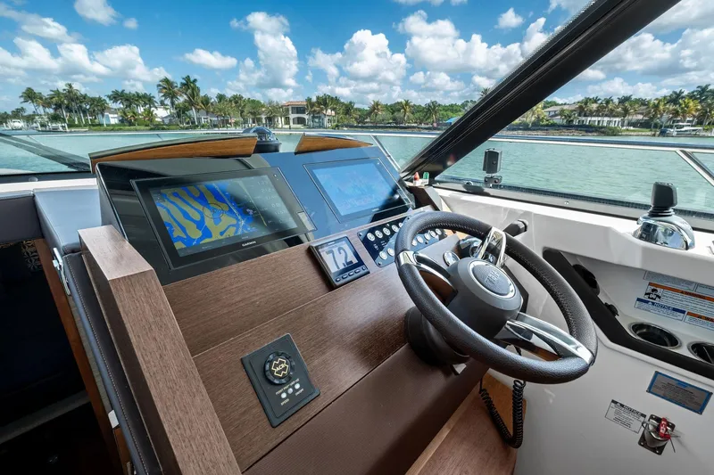 Slide: The Image of 2018 Tiara Yachts C44 Coupe helm with navigation screens and steering wheel, overlooking scenic waterway. - 51