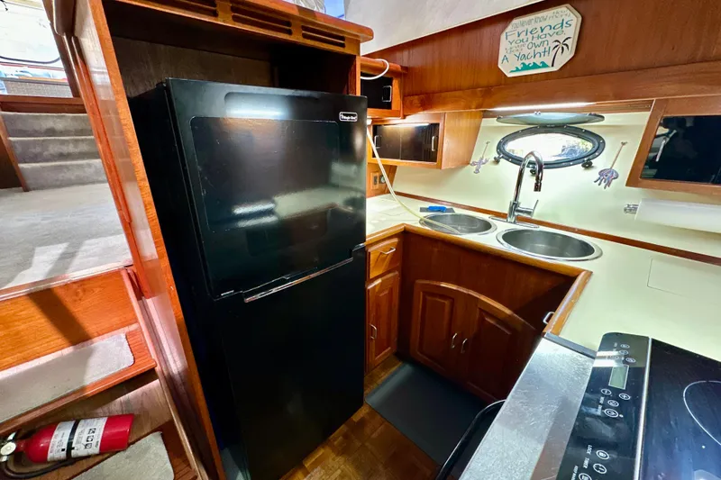 Slide: The Image of 1988 Californian 45 Motor Yacht kitchen with black fridge, dual sinks, and wooden cabinetry. - 15