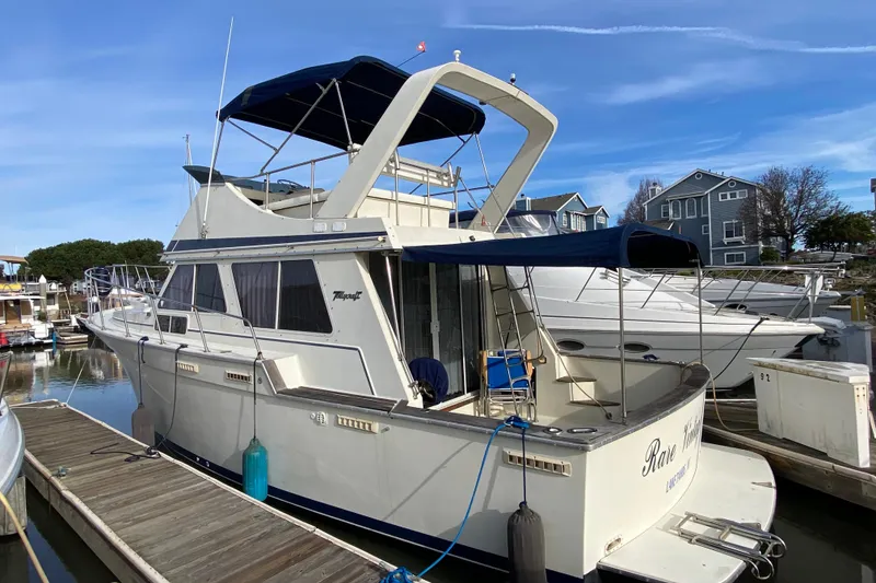 The Image of 1986 Tollycraft Flybridge Convertible docked at marina, featuring blue canopy and spacious deck. - 1