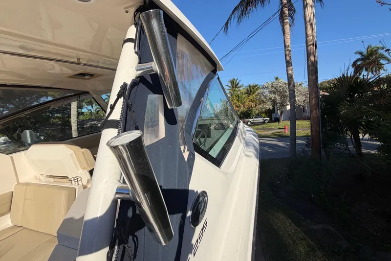 Slide: The Image of 2017 Pursuit DC 295 Dual Console boat with rod holders, parked near palm trees. - 37