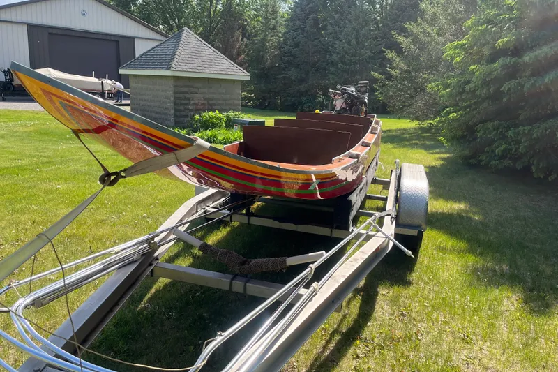 Slide: The Image of 1990 Utility Series Thai Longboat on trailer, parked on grassy lawn near buildings. - 10