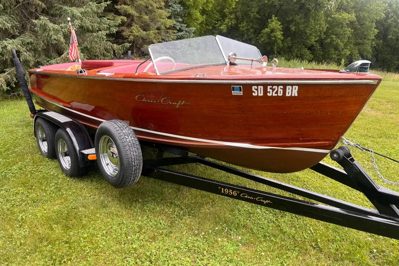 The Image of 1956 Chris-Craft 17 Sportsman boat on trailer, parked on grass with trees in background. - 1