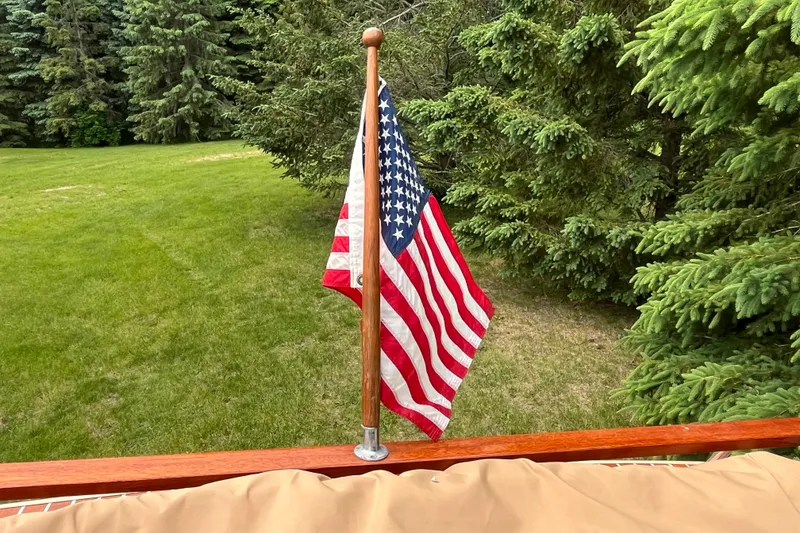 Slide: The Image of American flag on 1979 Skiff Craft 24 Flybridge, surrounded by lush green trees. - 32