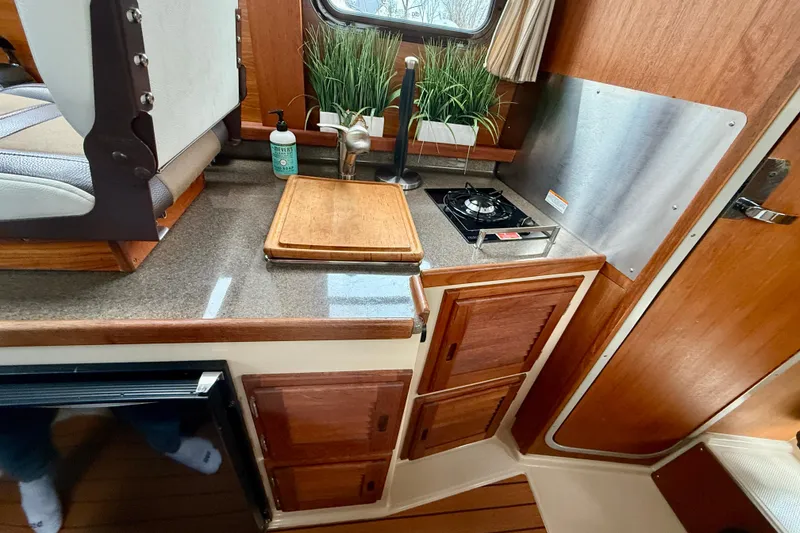 Slide: The Image of 2017 Ranger Tugs R-25 interior kitchen with stove, sink, and wooden cabinetry. - 13