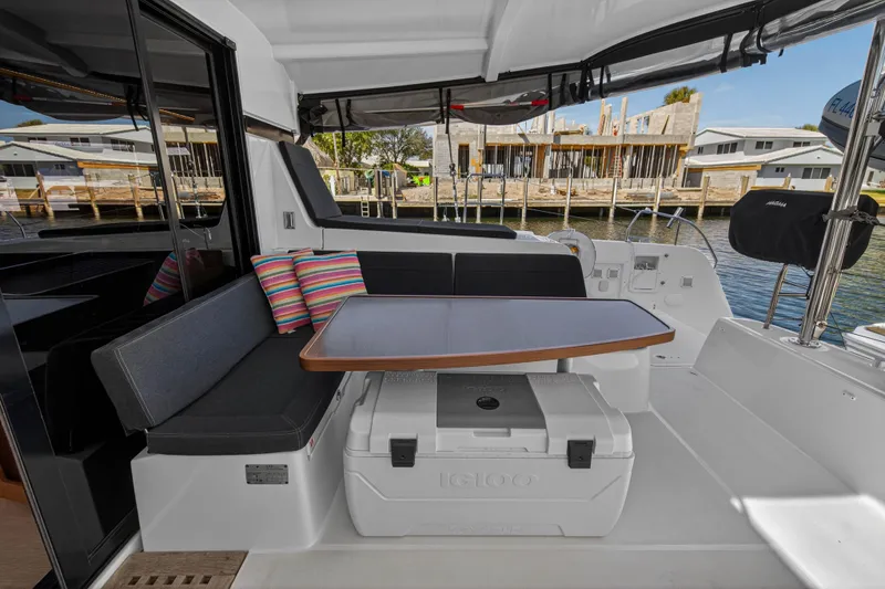 Slide: The Image of 2019 Lagoon 42 yacht cockpit with seating, table, and colorful cushions by the waterfront. - 18