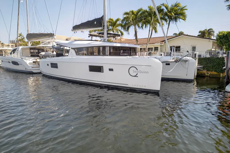 Slide: The Image of 2019 Lagoon 42 catamaran docked near palm trees and waterfront homes. - 2