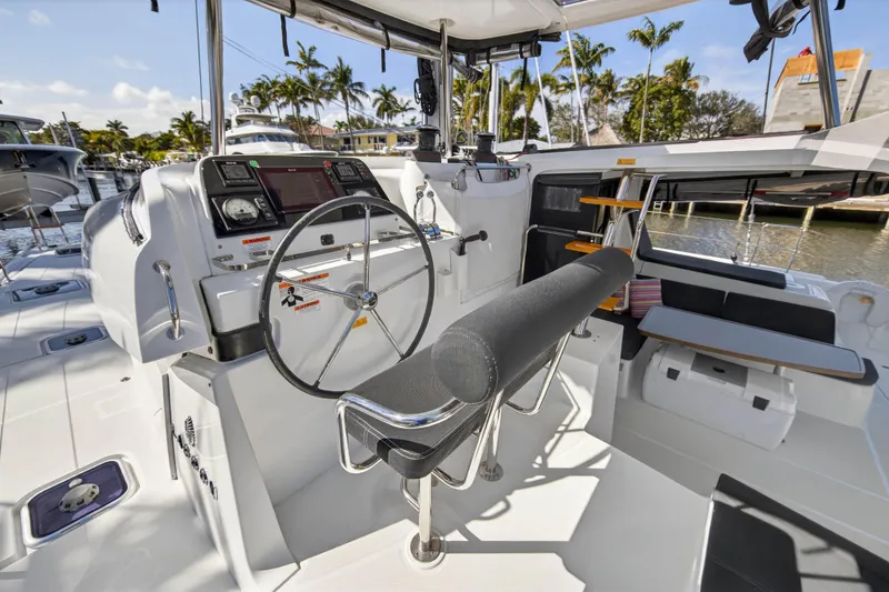 Slide: The Image of 2019 Lagoon 42 yacht cockpit with steering wheel, navigation controls, and seating, docked near palm trees. - 28