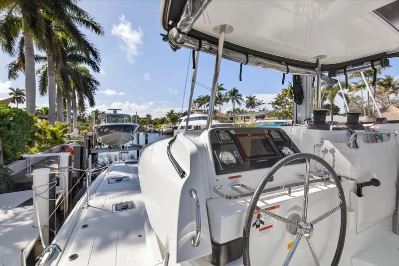 Slide: The Image of 2019 Lagoon 42 catamaran docked, featuring steering wheel and navigation controls, surrounded by palm trees. - 45