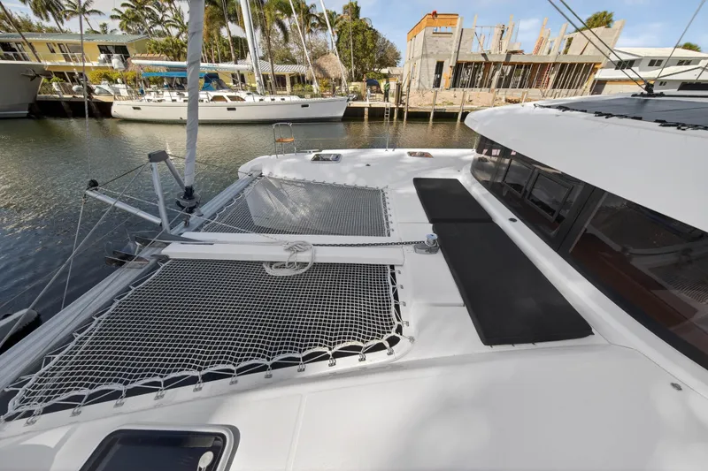 Slide: The Image of 2019 Lagoon 42 catamaran docked, featuring spacious deck and netting, with waterfront view. - 48