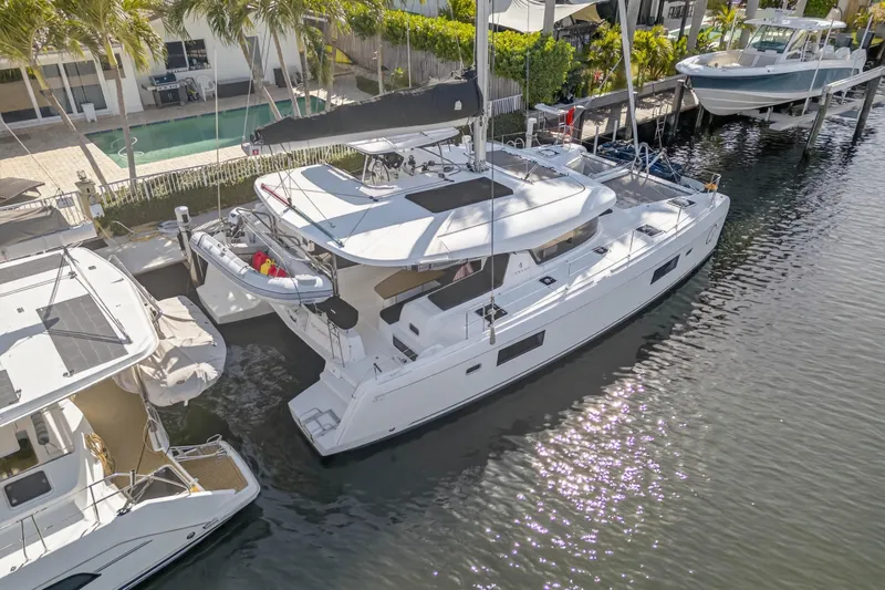 Slide: The Image of 2019 Lagoon 42 catamaran docked by waterfront homes, surrounded by palm trees. - 5