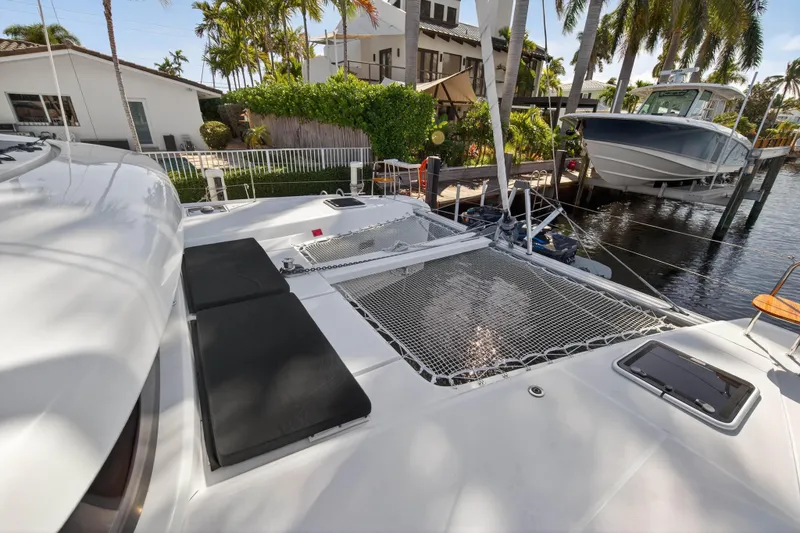 Slide: The Image of 2019 Lagoon 42 catamaran docked by waterfront homes, featuring spacious deck and netting. - 53