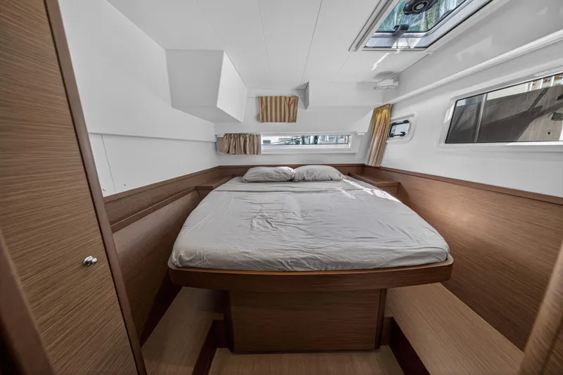 Slide: The Image of 2019 Lagoon 42 yacht cabin with a cozy bed, wooden interior, and natural light. - 93