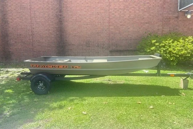 The Image of 2026 Tracker Grizzly 12 Jon boat on trailer, parked on grass near brick wall. - 0